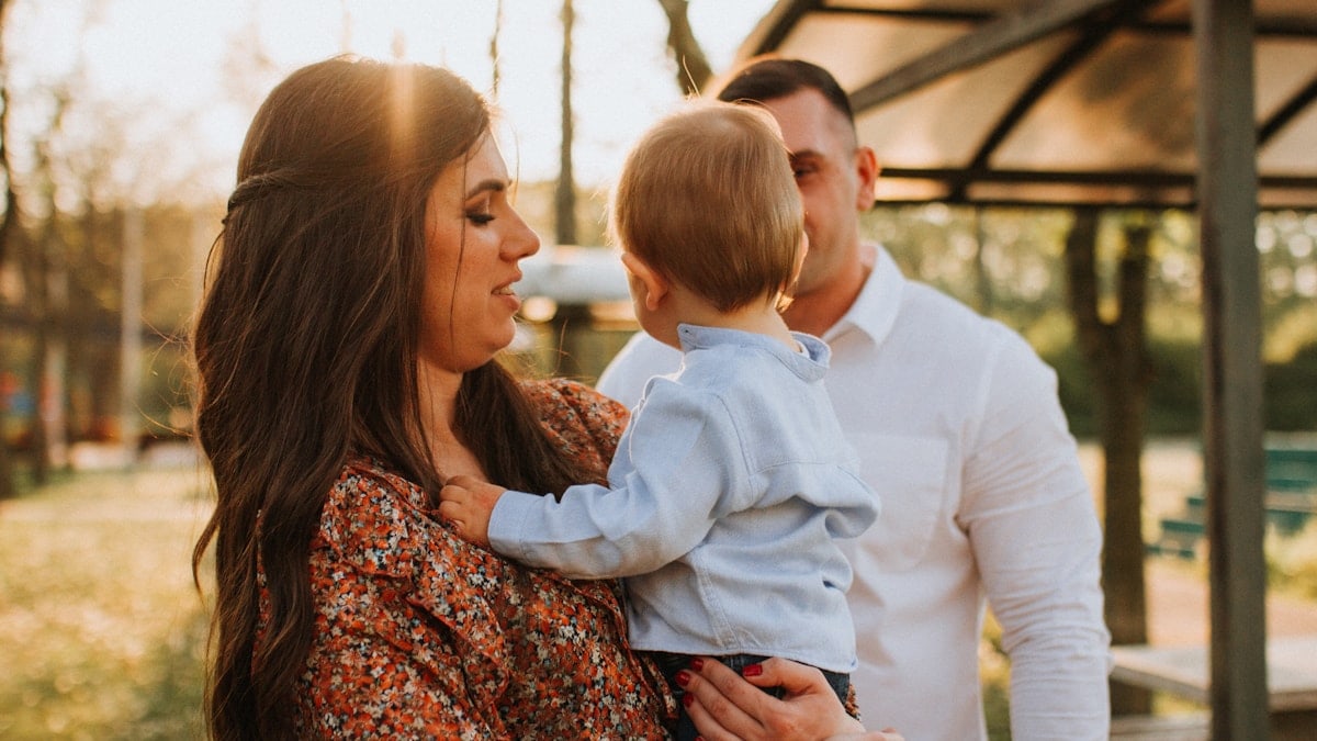 a man and woman holding a baby in a park